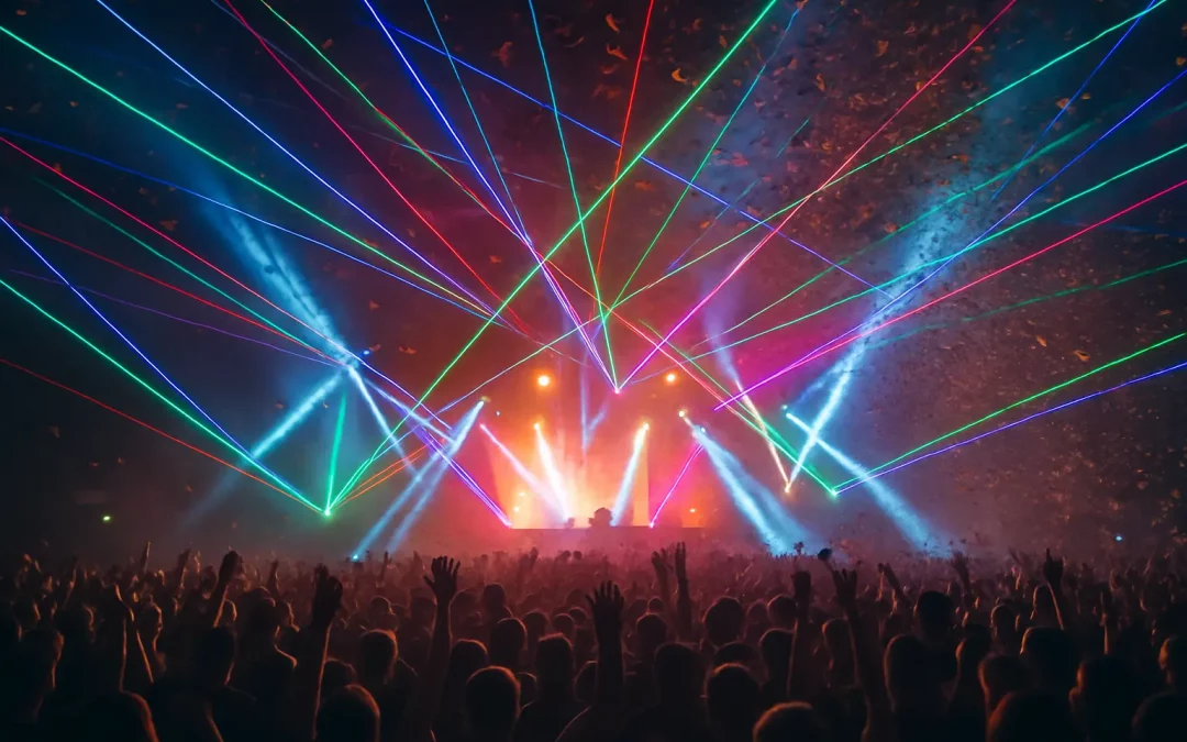 Eine riesige Menschenmenge steht vor einer hell erleuchteten Bühne, auf der bunte Laserstrahlen und Scheinwerfer durch neblige Luft schneiden. Konfetti wirbelt in der Luft, während zahlreiche Hände in die Höhe gereckt sind. Die Szene strahlt pure Partyatmosphäre aus – energiegeladen, farbenfroh und ganz klar: das Event des Jahres.